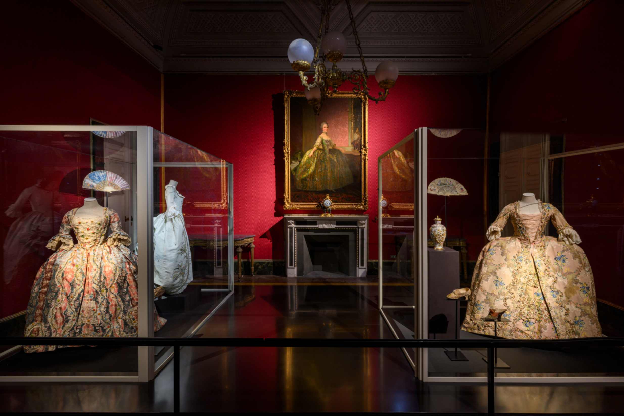 SALA 1: IL SETTECENTO, DA LUIGI XV ALL’ANCIEN RÉGIME Veduta d’insieme di tre abiti settecenteschi di manifattura italiana, due andrienne e una robe à la polonaise, un prezioso vaso (Manifattura di Meissen, 1720 ca.) e alcuni accessori coevi. Sulla parete il Ritratto di Maria Luisa di Borbone, futura Regina di Spagna di Laurent Pecheux (1765)