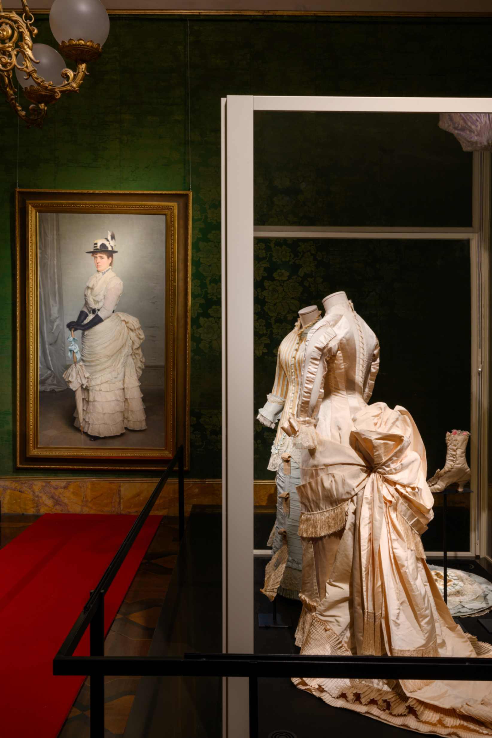 SALA 4 dettaglio: GLI ANNI SETTANTA E OTTANTA DELL’OTTOCENTO Due abiti da sposa databili agli anni Settanta e Ottanta dell’Ottocento, uno in raso e gros di seta avorio di Charles Frederick Worth e l’altro in ‘style tapissier’ in seta operata a righe con guarnizioni in taffetas, merletto, gros e tulle. Sulla parete il Ritratto di Signora con vestito in Plumetis di Tito Conti (1878-80)