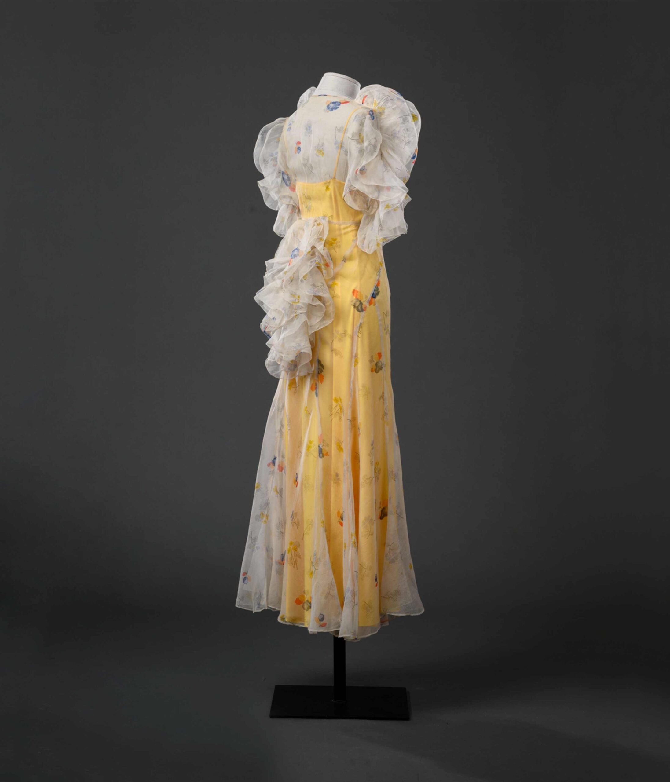 SARTORIA FIORENTINA ABITO FEMMINILE 1935 circa Abito garden party in organza di seta avorio stampata a motivi floreali grigi, rossi, gialli e blu. Maniche e retro abito decorate con rouches a “farfalla”. Sottabito in duchesse giallo canarino. Peonia in seta avorio applicata su spalla destra. Collezione Massimo Cantini Parrini, Firenze